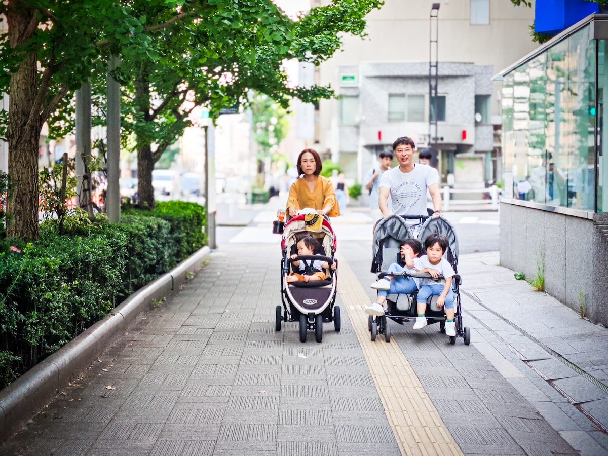 Two families walking their strollers down a tree-lined sidewalk